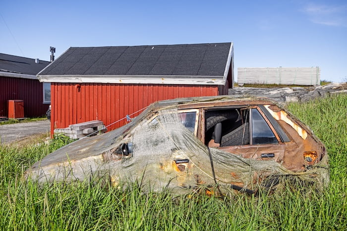 old broken down car covered with a decaying tarp outside of red residential buildings