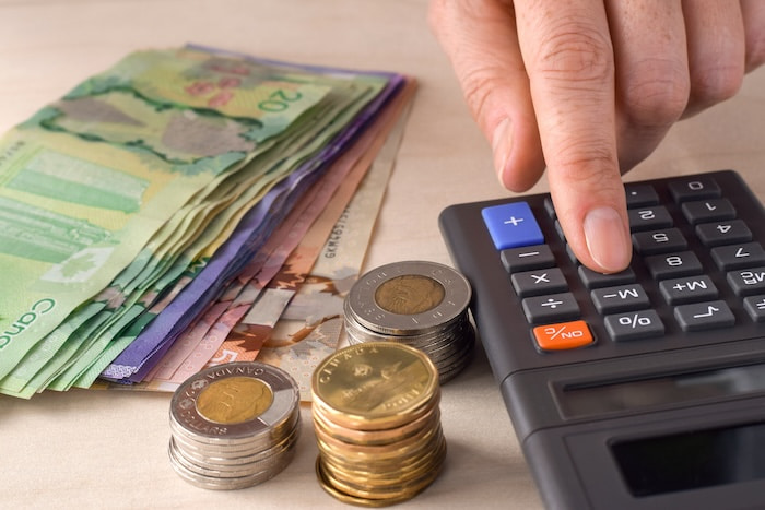 Person punching numbers on an old-school calculator with Canadian dollar bills and coins sitting next to them on a table